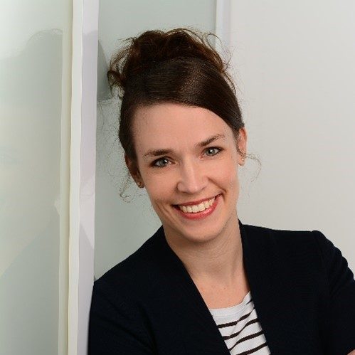 Lächelnde Frau mit schulterlangen brünetten Haaren, gestreiftem Shirt und schwarzem Blazer. psychiatrische häusliche Krankenpflege