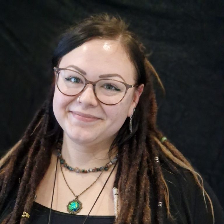 Junge Frau mit Dreadlocks und Brille, lächelt vor schwarzem Hintergrund. ambulante psychiatrische Krankenpflege