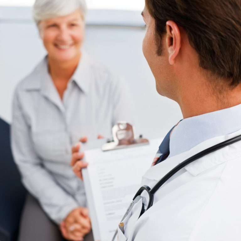 Arzt spricht mit lächelnder Patientin, hält ein Clipboard in der Hand. häusliche Krankenpflege