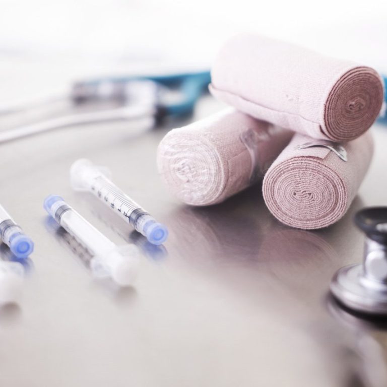Rollen von Bandagen und Spritzen auf einer Oberfläche, im Hintergrund ein Stethoskop. häusliche Krankenpflege