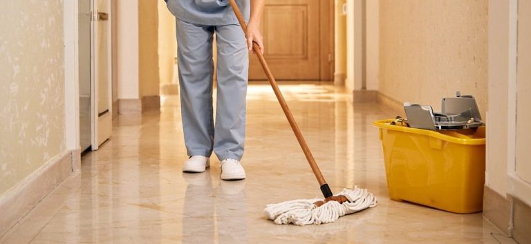 Eine Person wischt einen glänzenden Flur mit einem Mop und einem Eimer daneben.